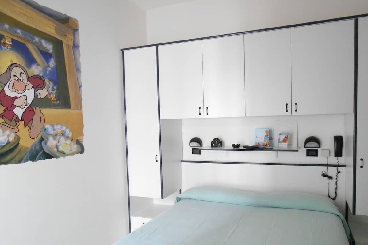 A bedroom with a bed, a white wardrobe, a shelf with items, a clock, and a telephone.