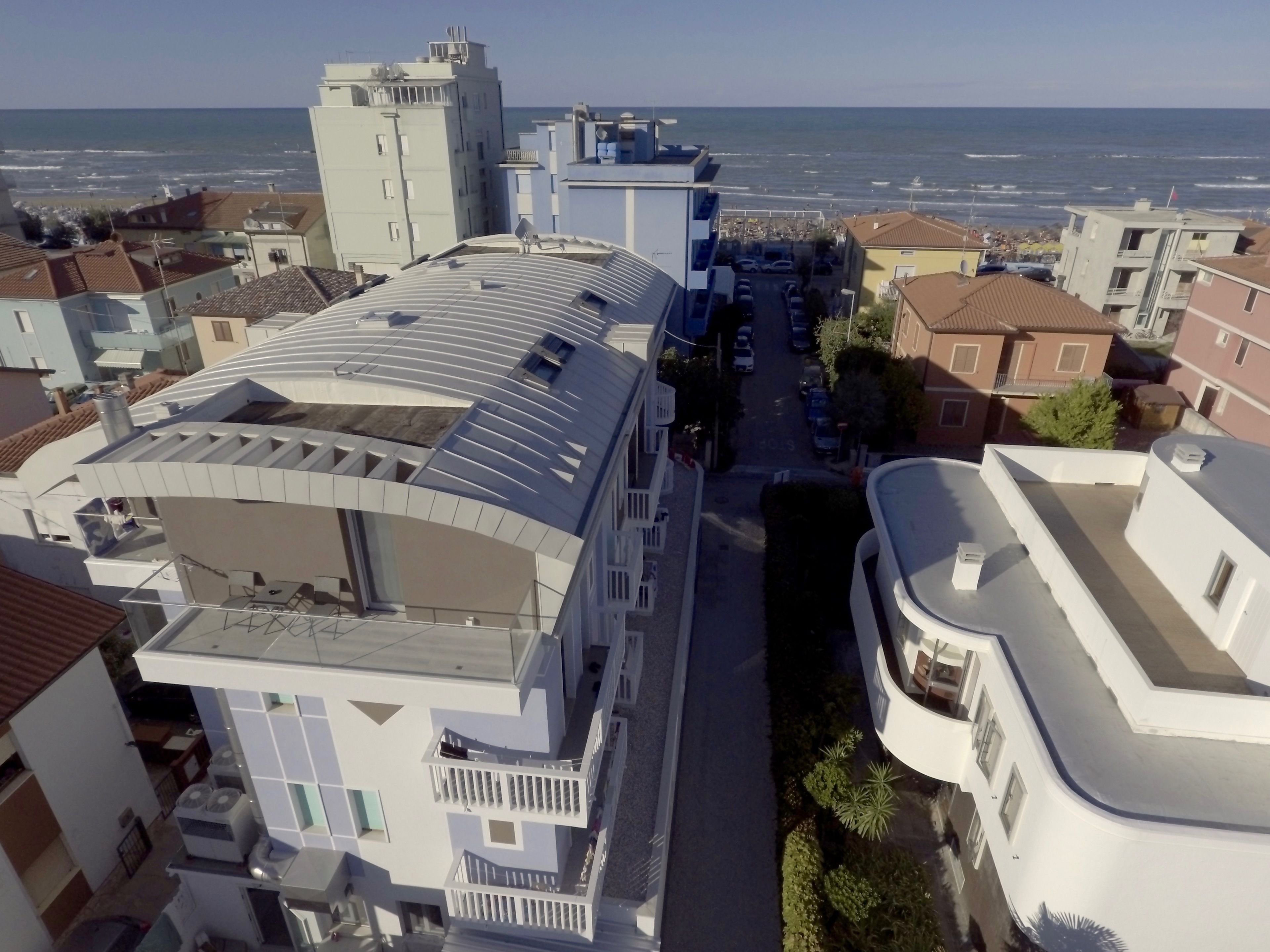 A modern building with a curved roof and multiple balconies, overlooking a coastal area with a view of the sea.