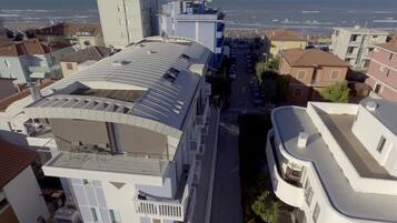 Um edifício moderno com telhado curvo e várias varandas, com vista para uma área costeira e o mar.