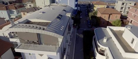 A modern building with a curved roof and multiple balconies, overlooking a coastal area with a view of the sea.
