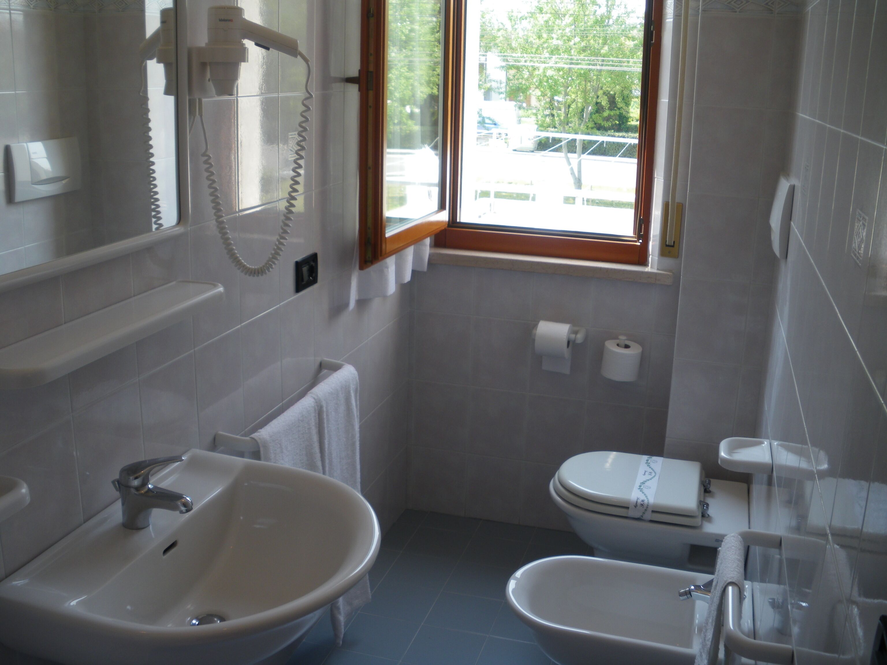 Ein Badezimmer mit Waschbecken, Bidet, Toilette und einem Fenster mit Blick ins Freie.