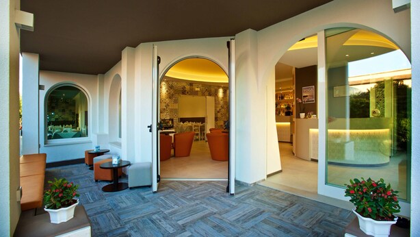 A modern hotel lobby with a herringbone-patterned floor, seating areas, and glass doors leading to a dining area. - Hotel Biancaneve (Mondolfo)