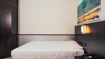 Una habitación de hotel moderna con una cama, una mesita de noche, un cuadro y una lámpara de pared.