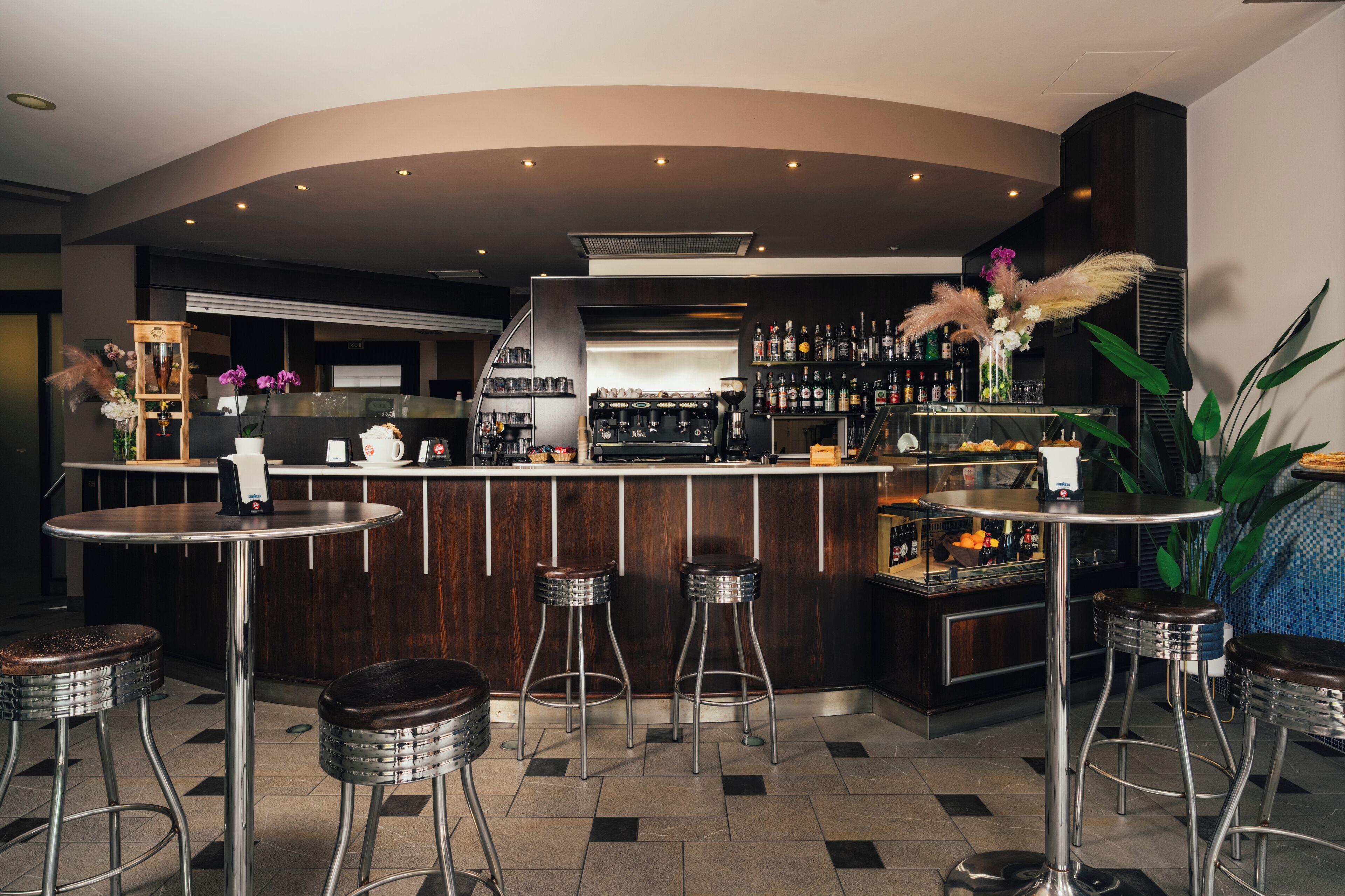 A bar area with a curved counter, stools, and a variety of bottles and glasses.