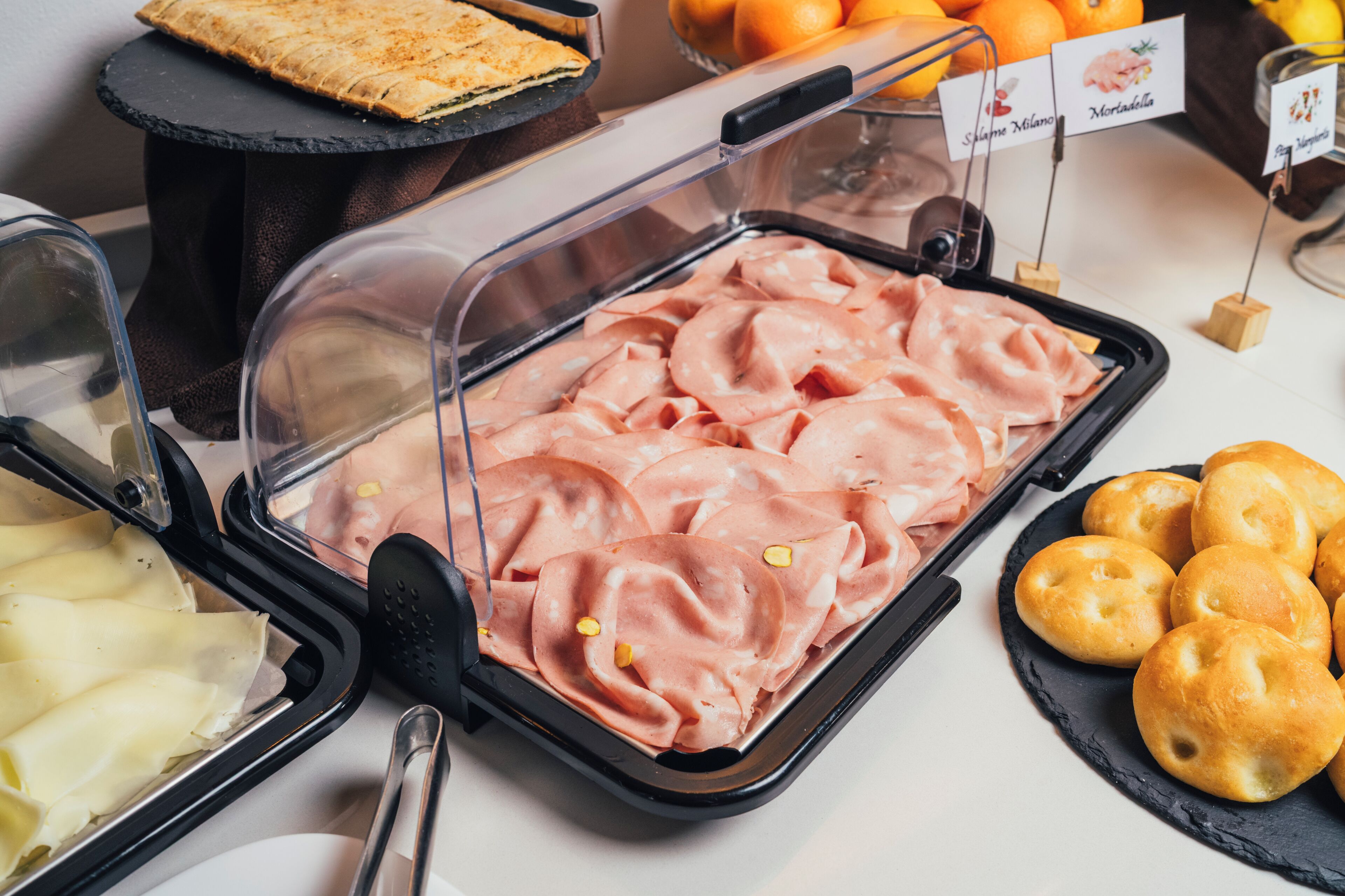 Un buffet con diversi cibi, tra cui salumi, pasticcini e una selezione di frutta.