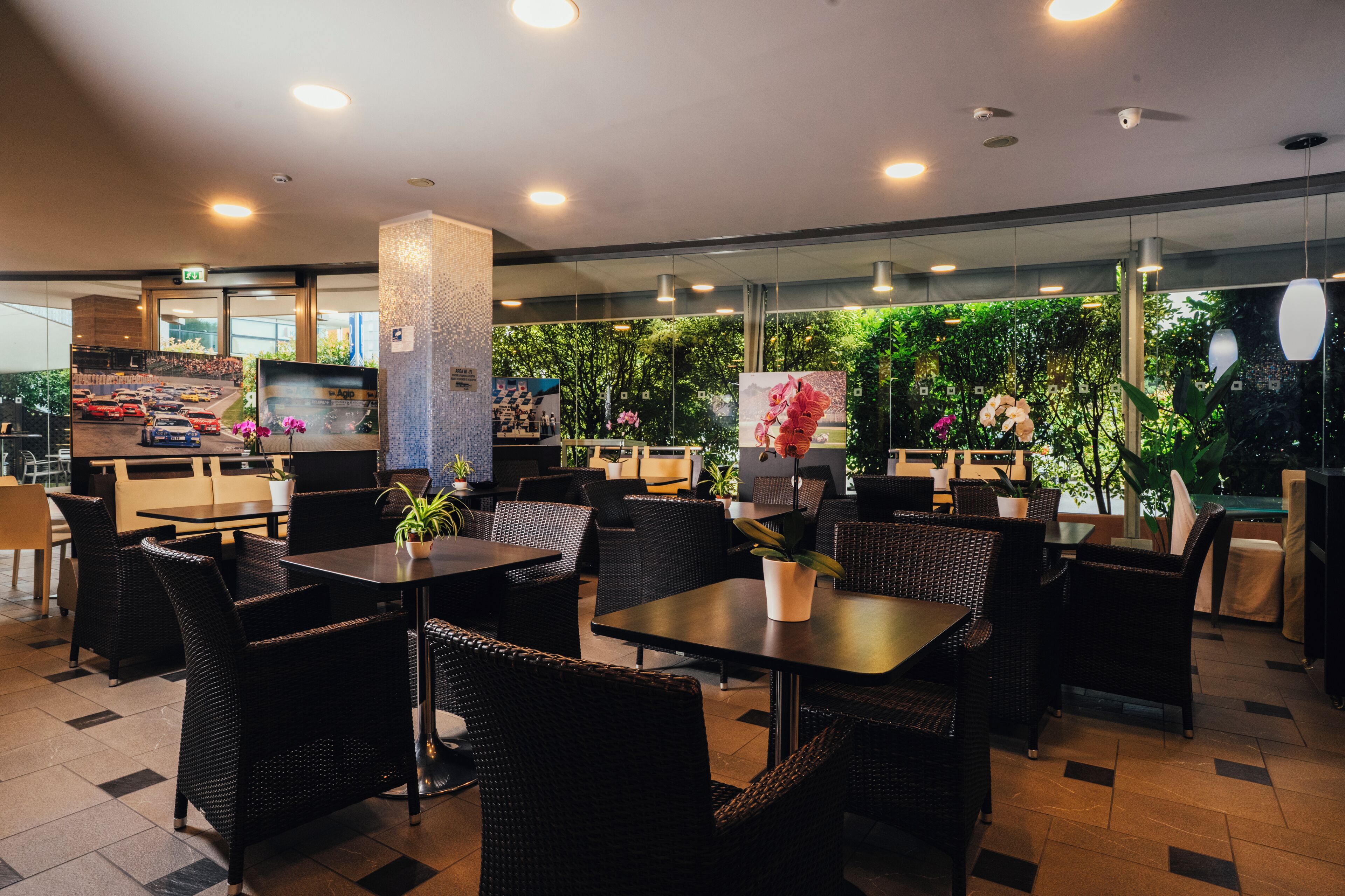 Um restaurante moderno com móveis de vime, plantas e uma grande janela com vista para o verde.
