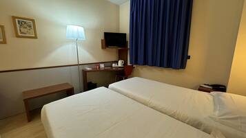 Een hotelkamer met twee bedden, een bureau met stoel, een televisietoestel en een raam met blauwe gordijnen.