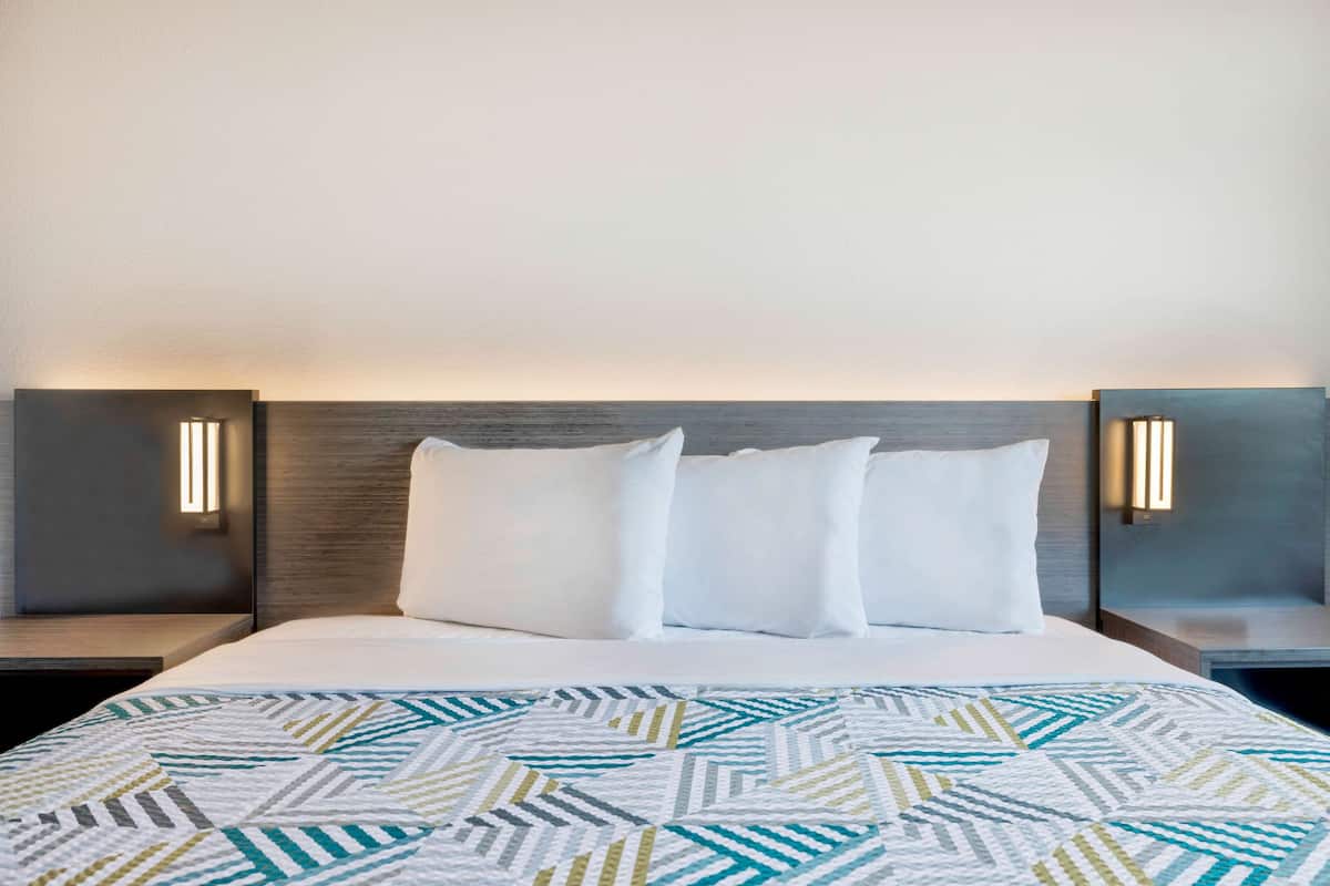 A hotel room with a large bed, two bedside tables, and wall-mounted lamps.