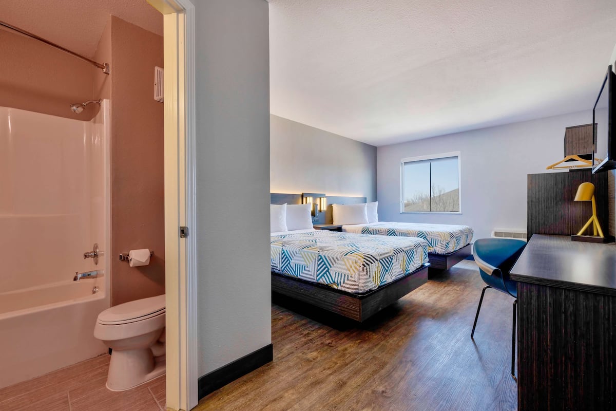 A modern bedroom with two beds, a desk, and a bathroom with a bathtub and toilet.