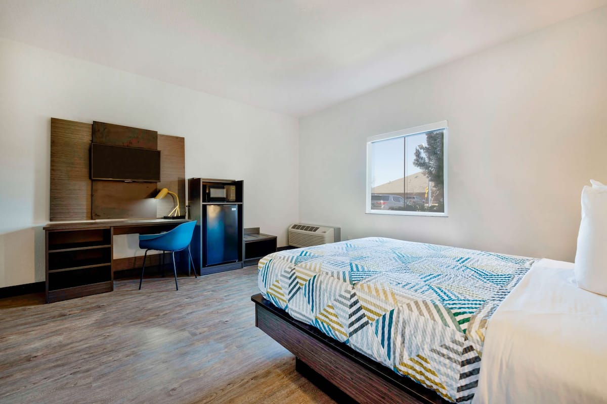 A bedroom with a bed, a desk, a chair, a TV, and a window.
