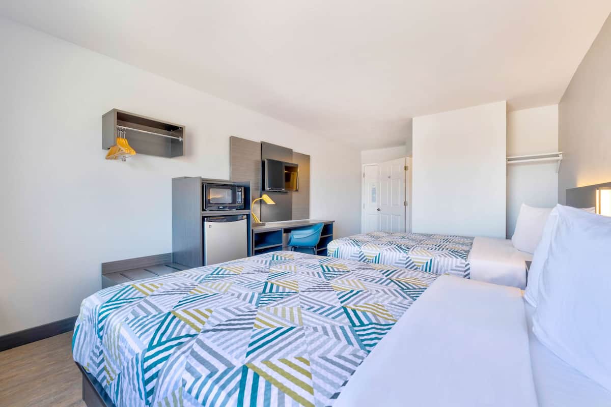 A hotel room with two beds, a desk with a computer, a microwave, and a wardrobe.