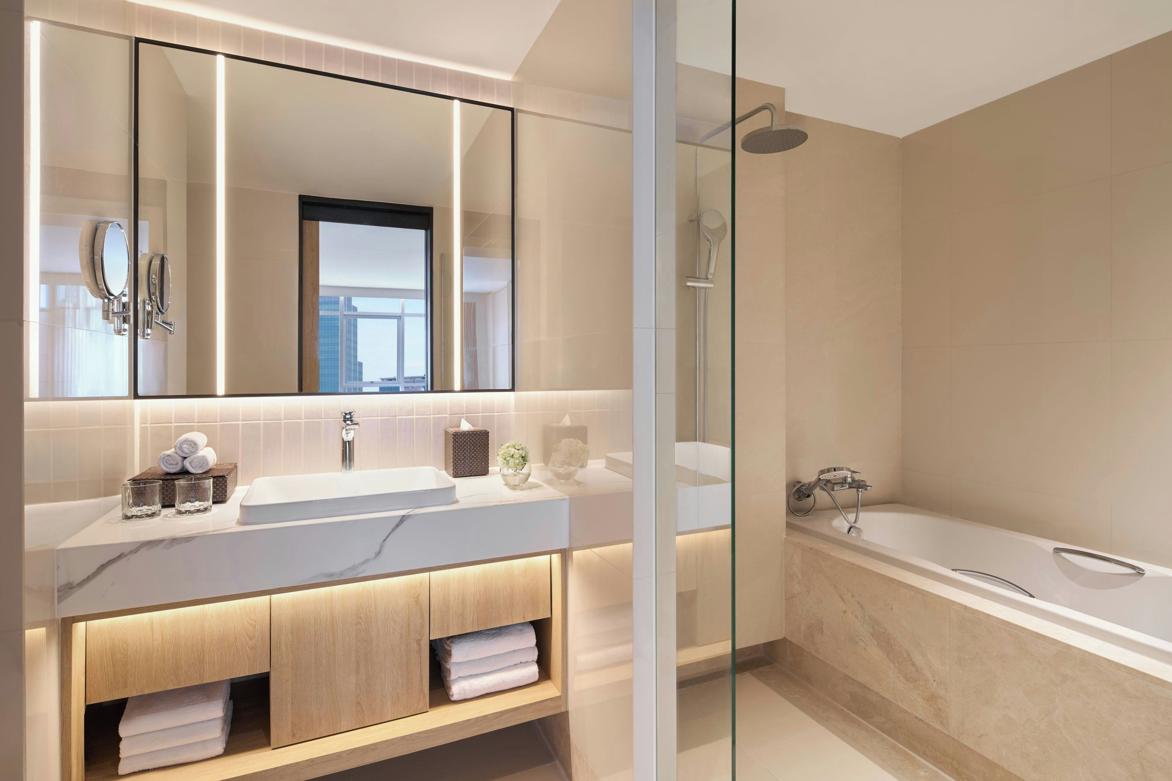 Une salle de bain moderne avec un grand miroir, deux lavabos, une douche et un espace de douche clos par des parois de verre.