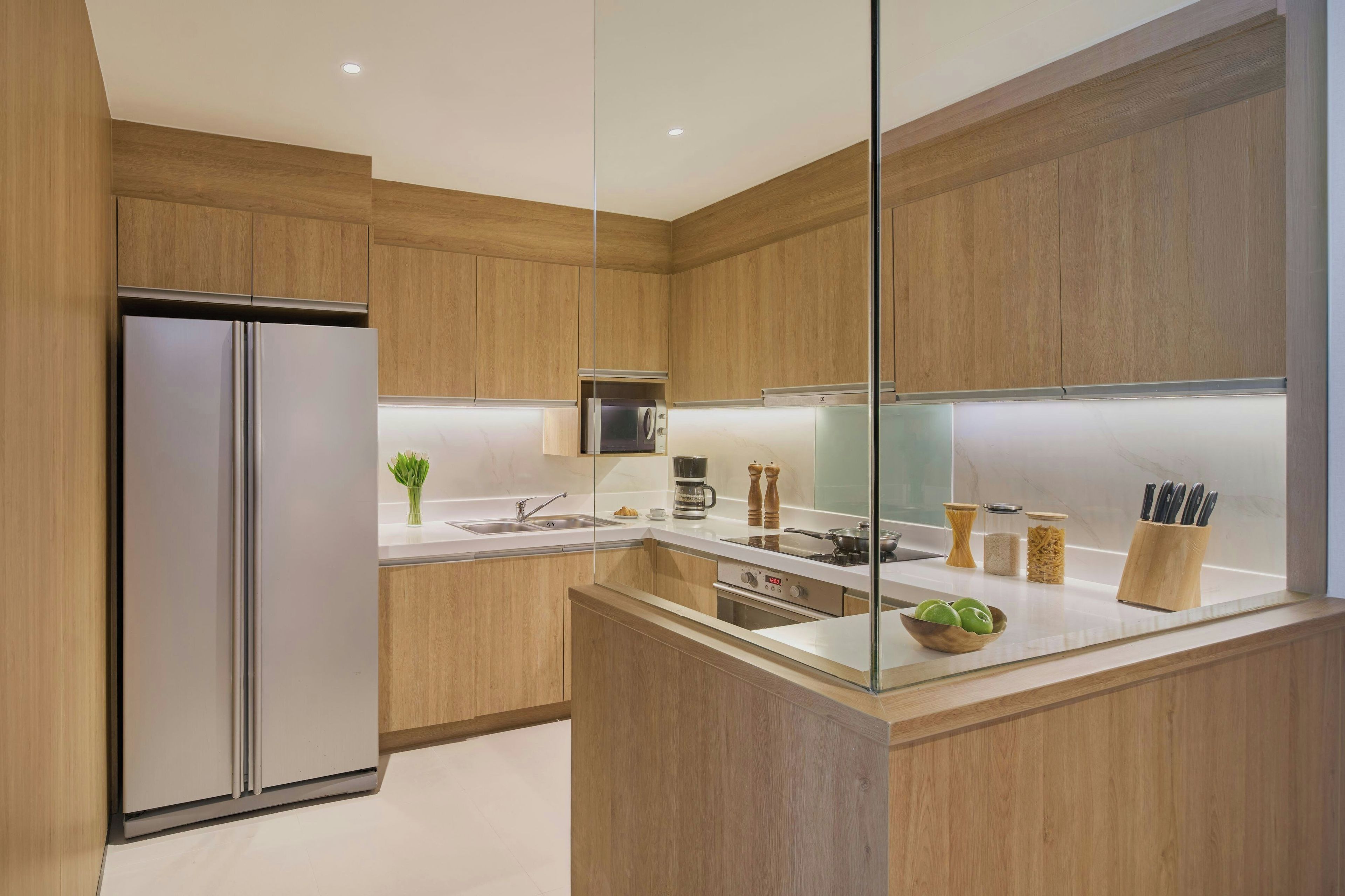 A modern kitchen with wooden cabinets, a stainless steel refrigerator, a built-in oven, and a countertop with various kitchen items.