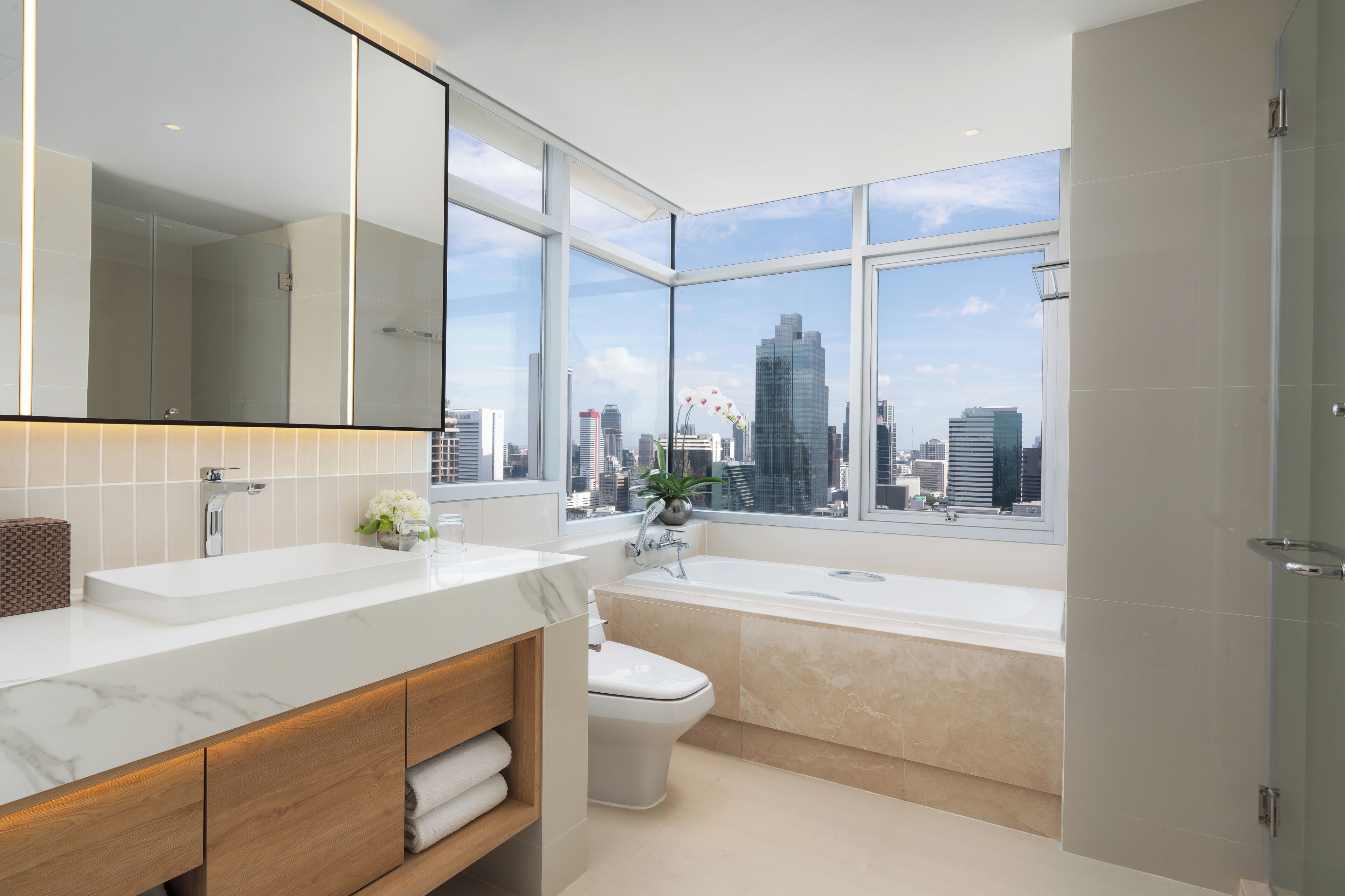 Ein modernes Badezimmer mit großem Fenster, einer Badewanne, einer Toilette und einem Waschtisch mit Spiegel.
