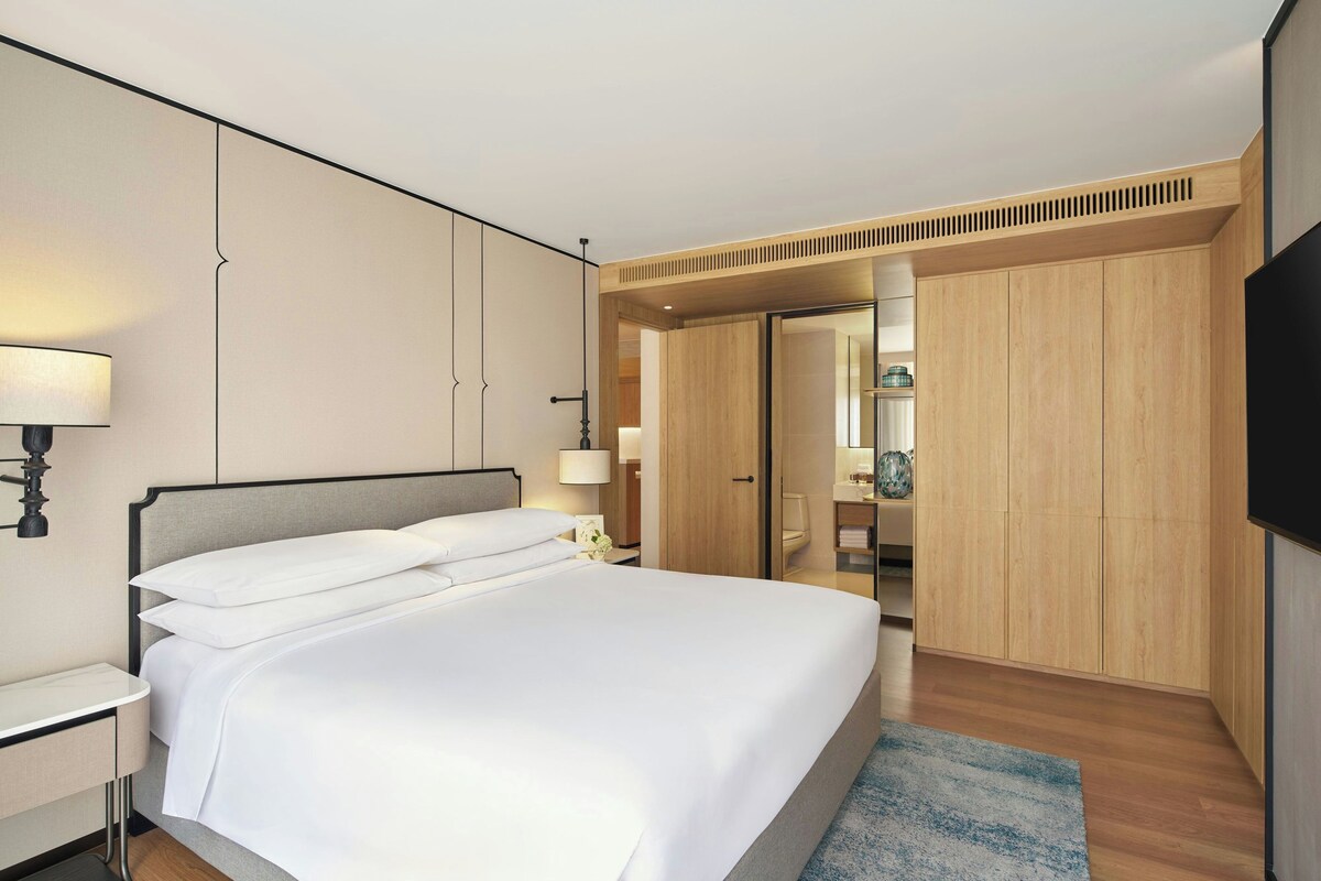 A hotel room with a bed, bedside table, lamp, wardrobe, and a television.
