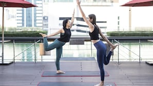 Twee personen doen yoga op matten, met een stadsgezicht op de achtergrond.