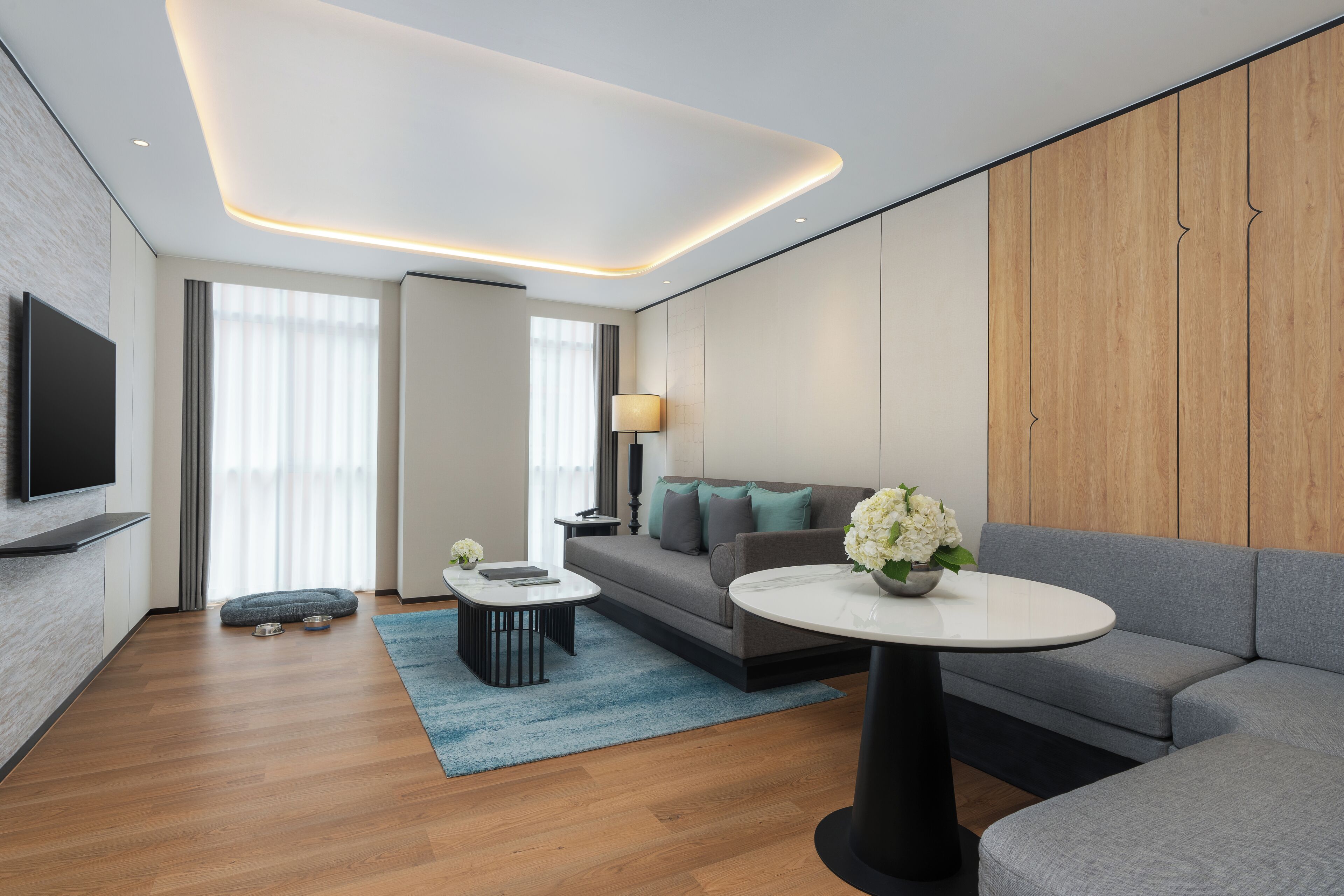 Un salon moderne doté d’un téléviseur à écran plat, d’un canapé gris, d’une table basse ronde et d’un mur décoratif en bois.