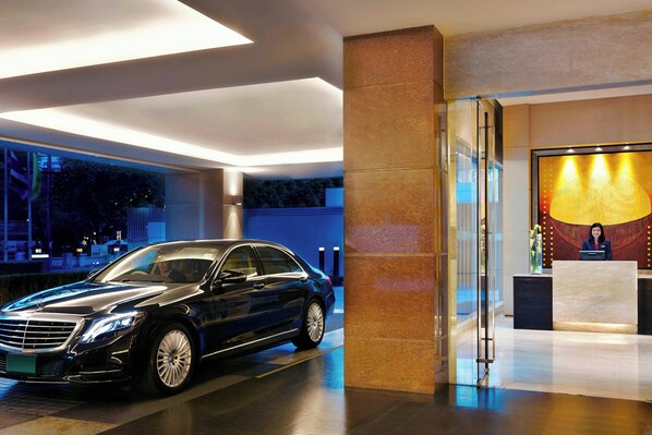 A luxury car parked inside a modern hotel lobby with a reception desk and a large illuminated artwork on the wall. - Sathorn Vista, Bangkok - Marriott Executive Apartments (Bangkok)