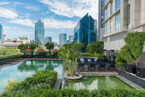A pool area with lounge chairs and umbrellas, surrounded by greenery and modern buildings in the background. - Sathorn Vista, Bangkok - Marriott Executive Apartments (Bangkok)
