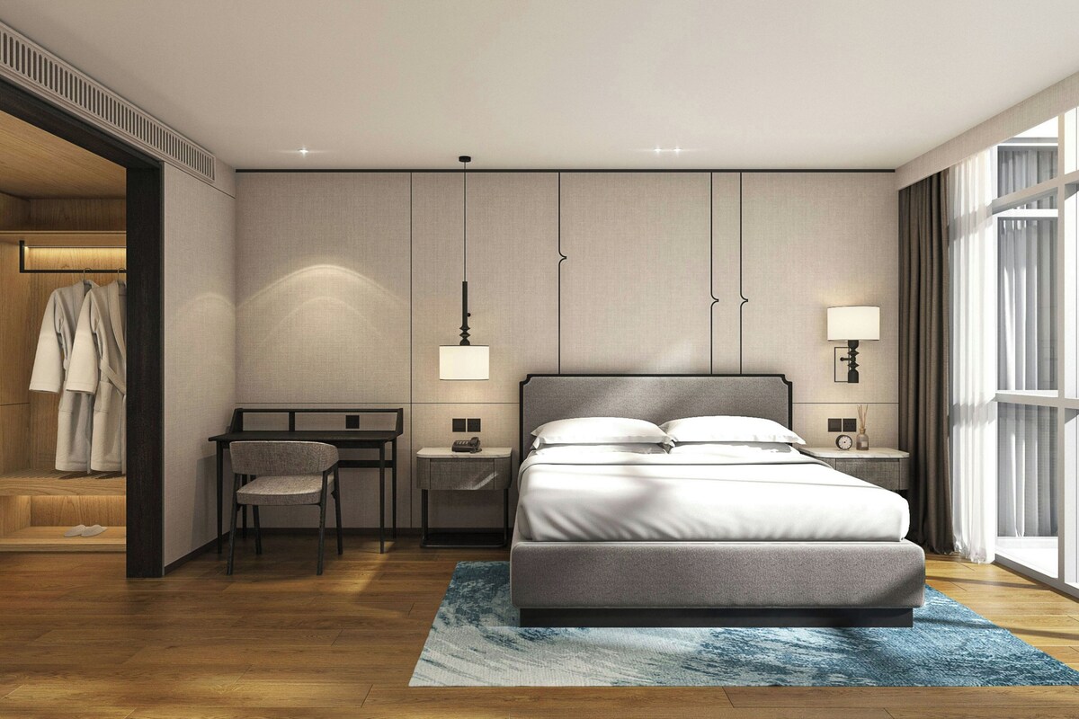 A modern hotel room with a bed, desk, chair, and wardrobe.