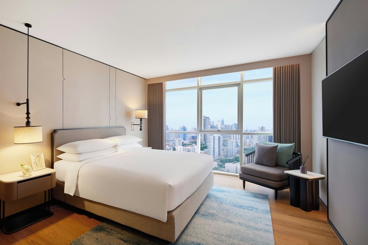 A modern hotel room with a large bed, a sitting area, and a city view.