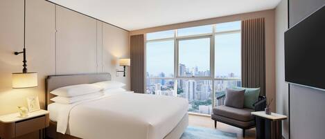 Una habitación de hotel moderna con una cama grande, zona de estar y vistas a la ciudad.