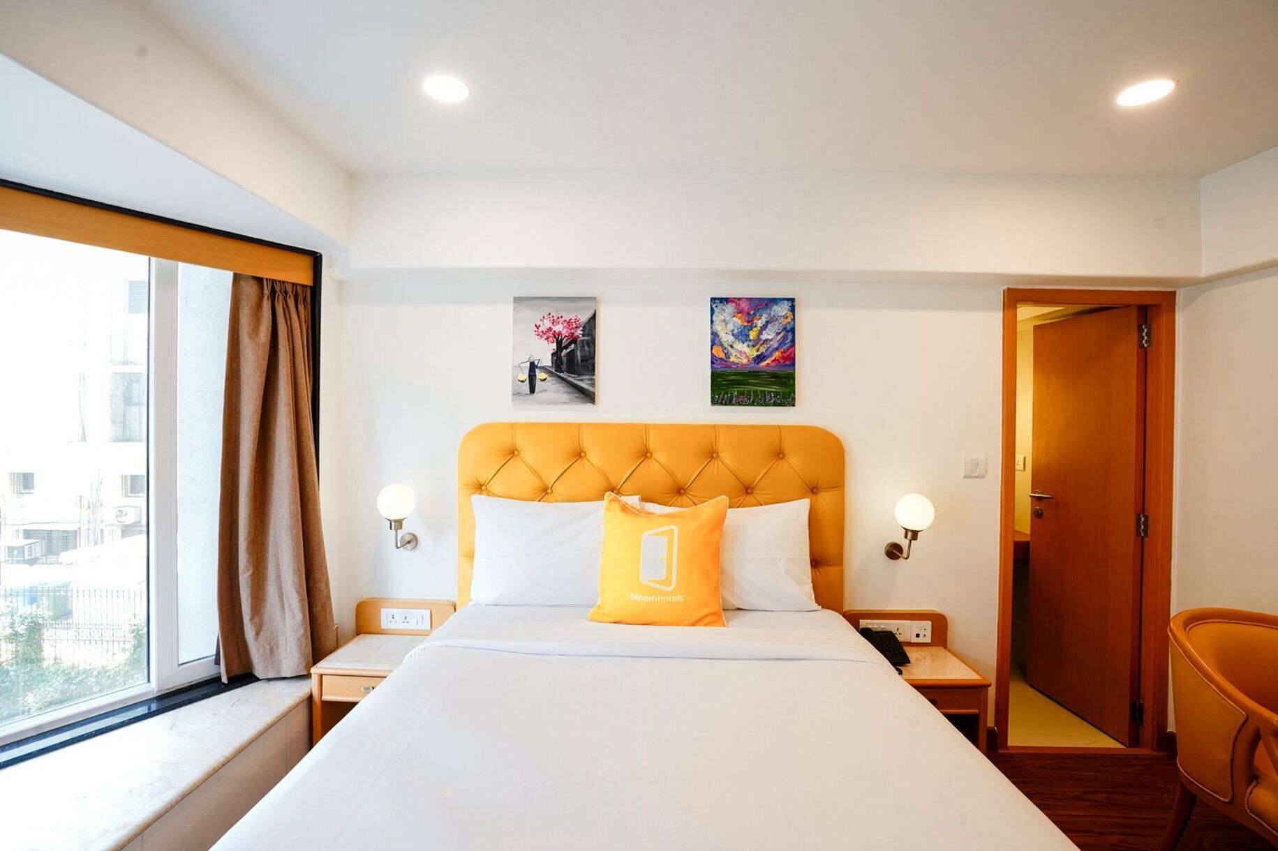 Une chambre d’hôtel avec un grand lit, deux lampes fixées au mur, une fenêtre avec des rideaux et une porte donnant sur une autre pièce.