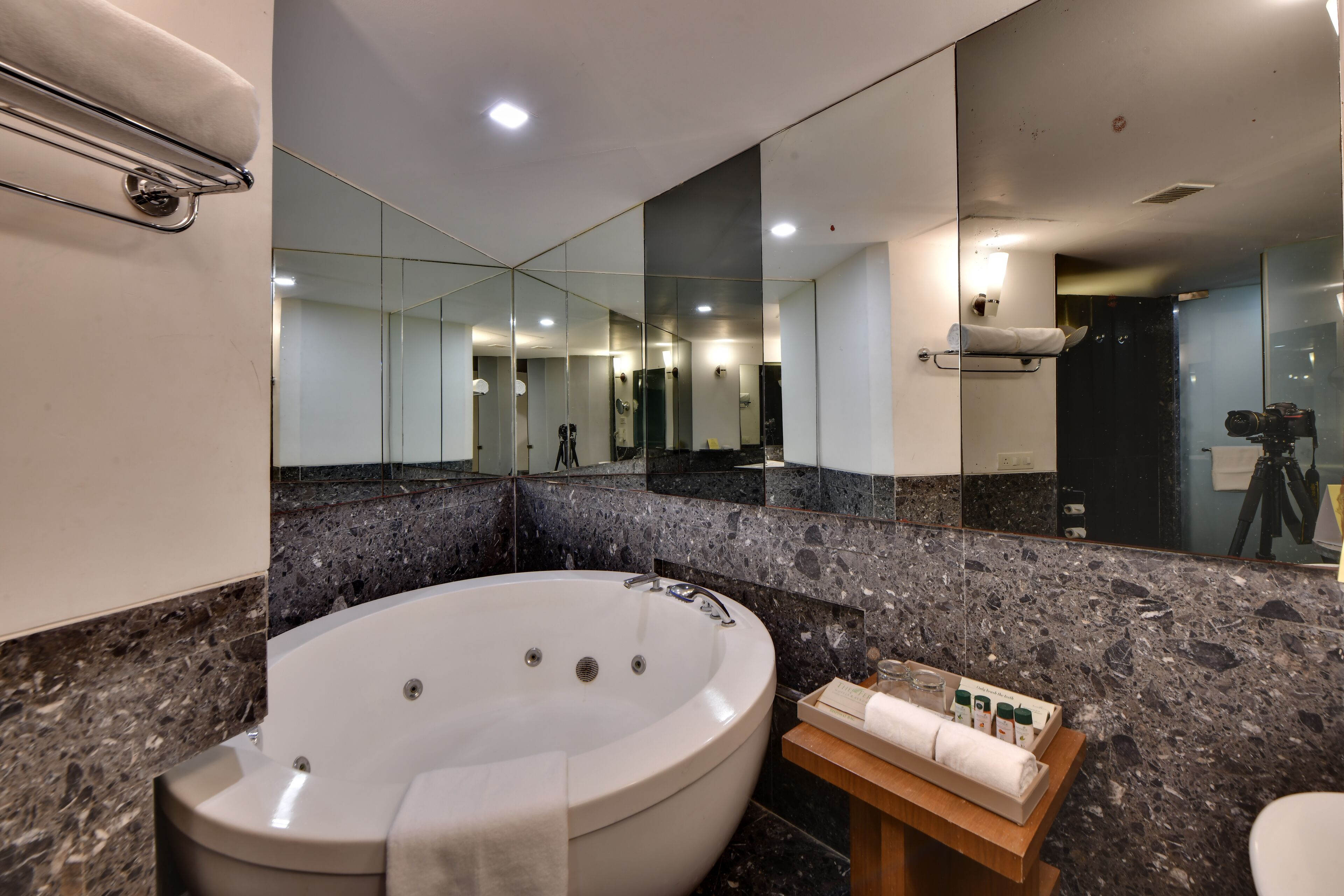 A modern bathroom with a large oval bathtub, a wooden side table with toiletries, and a mirror reflecting the room.