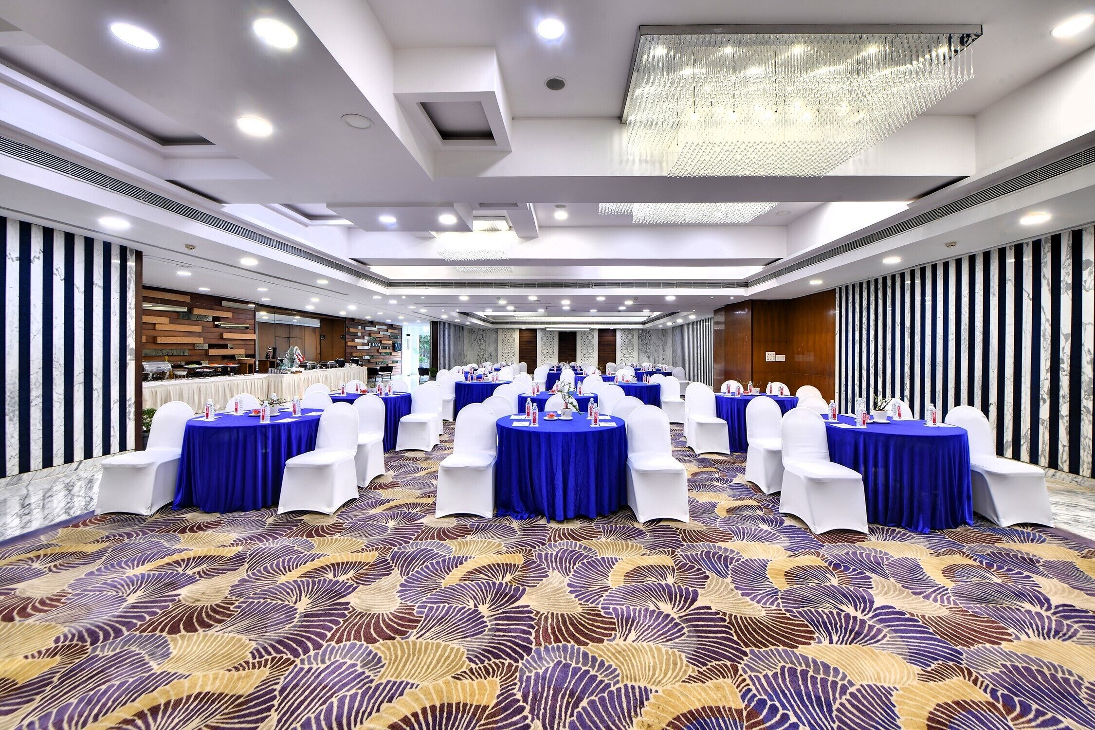 A banquet hall with round tables covered in blue tablecloths, white chairs, and a patterned carpet.