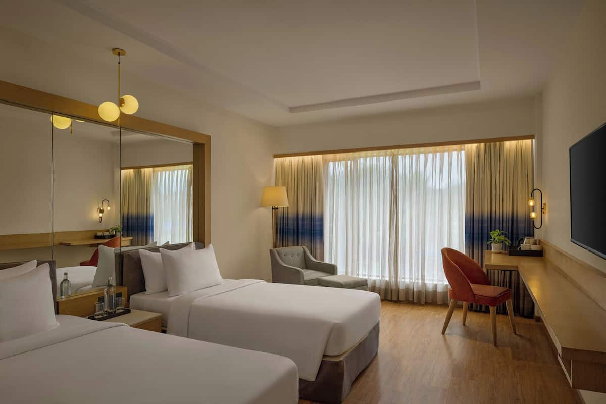 Een hotelkamer met twee bedden, een bureau, een stoel, een grote spiegel en een televisie.