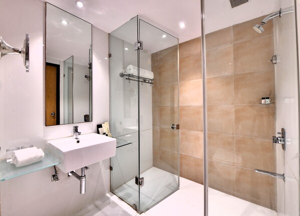 Un baño moderno con cabina de ducha de vidrio, un lavabo blanco y un espejo grande.