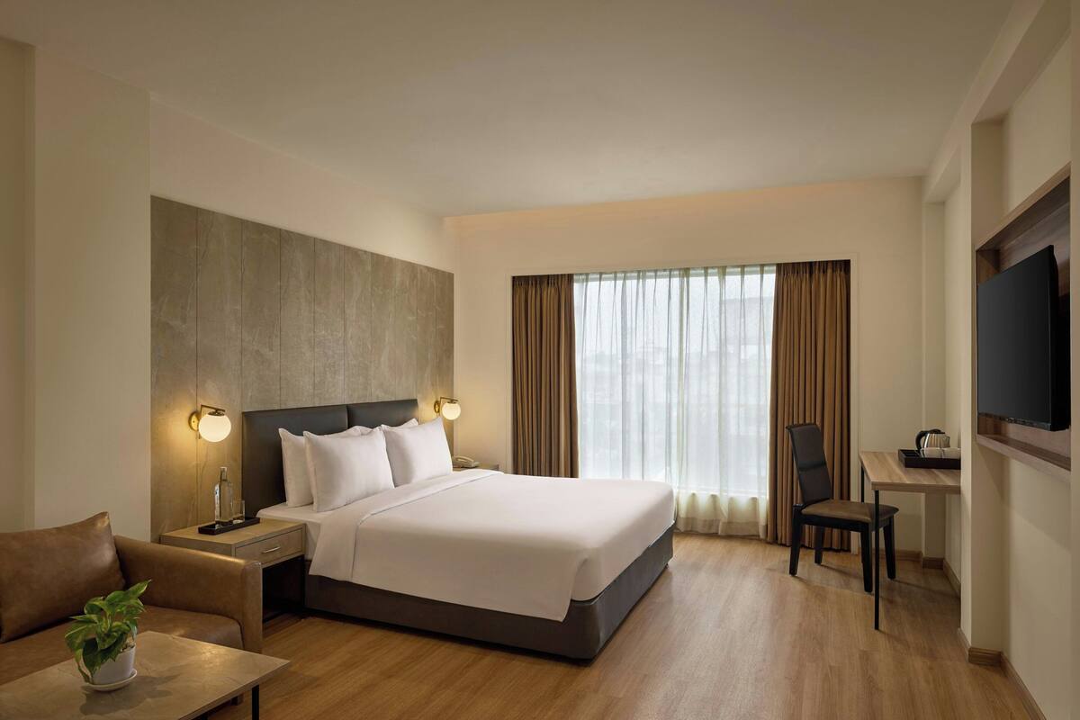 Een hotelkamer met een groot bed, een bureau, een stoel, een televisie en een potplant.