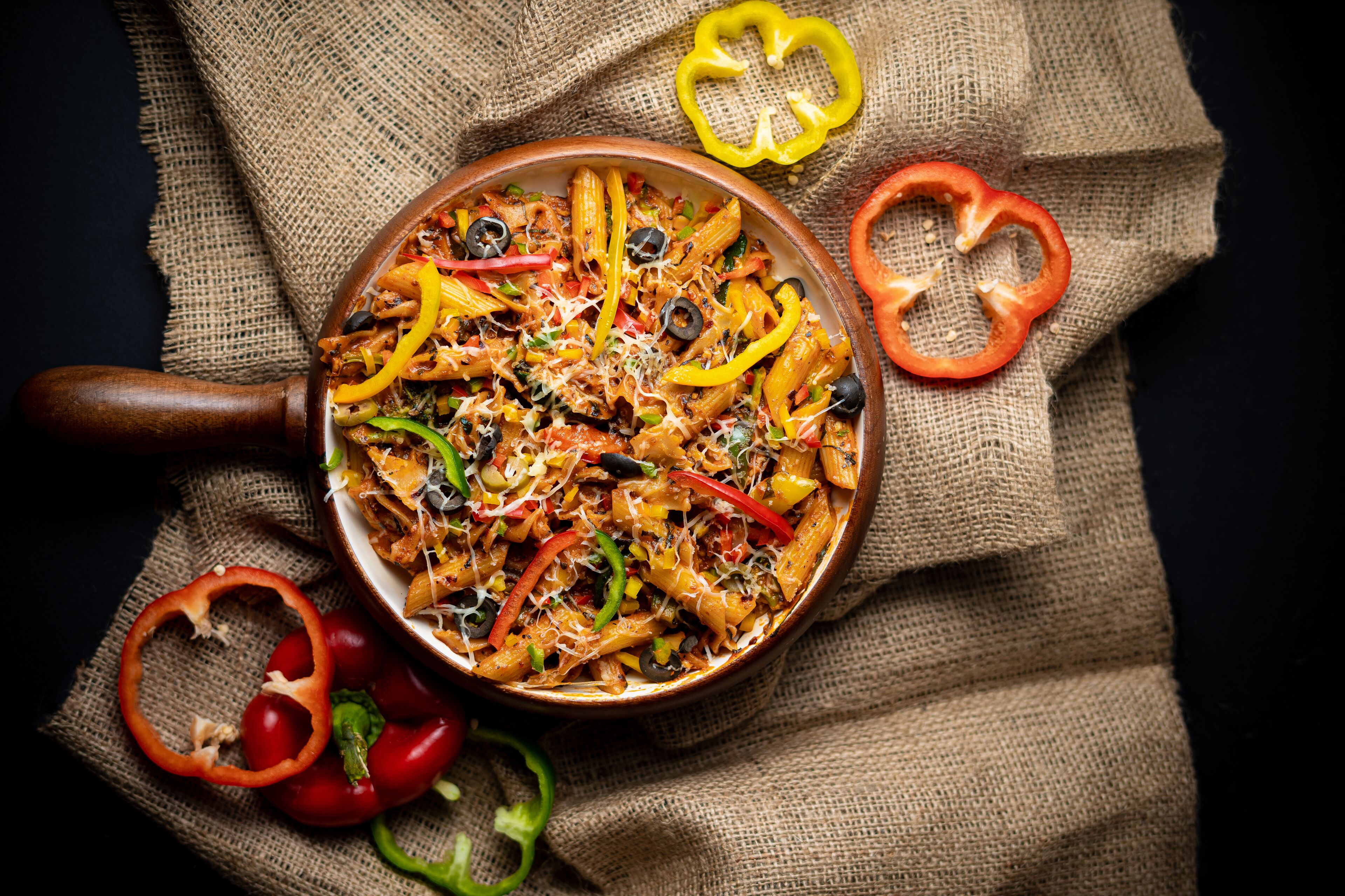 Una cazuela de pasta con verduras y queso sobre un lienzo de arpillera.