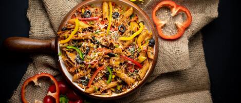 A pan of pasta with vegetables and cheese on a burlap cloth.