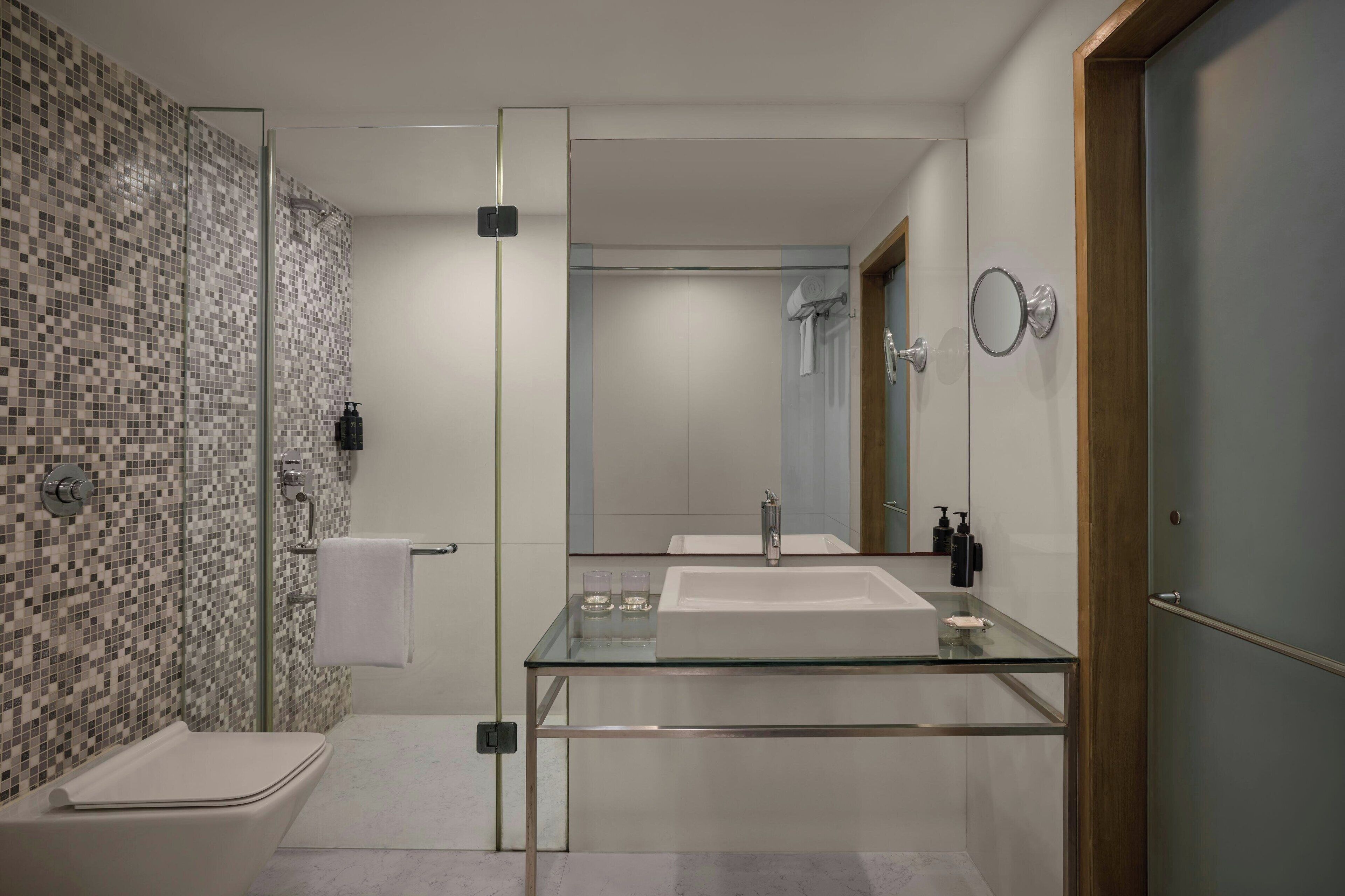 A modern bathroom with a glass vanity, a shower, and a tiled wall.