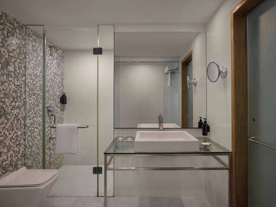 A modern bathroom with a glass vanity, a shower, and a tiled wall.