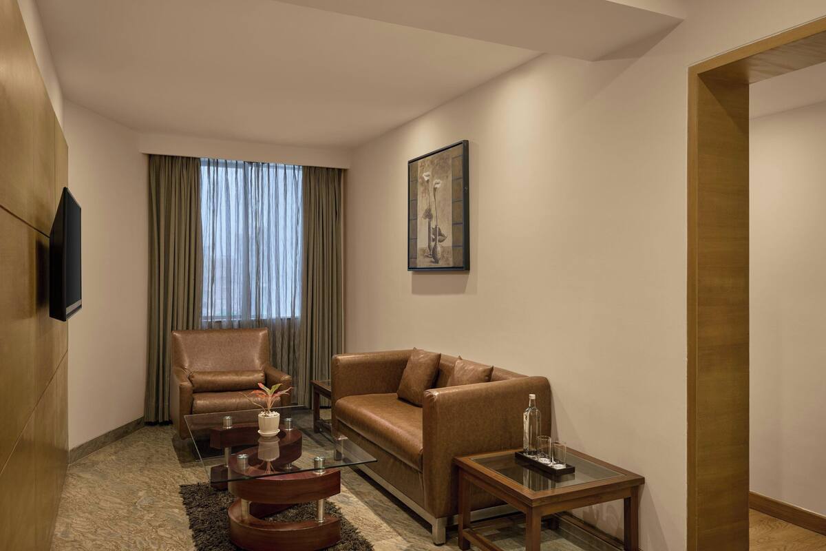 Een moderne woonkamer met een bruine leren bank, een glazen salontafel, een fauteuil van leer en een flatscreen televisie aan de muur.