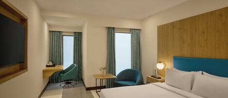 A hotel room with a large bed, a desk with a chair, a TV, and a window with curtains.