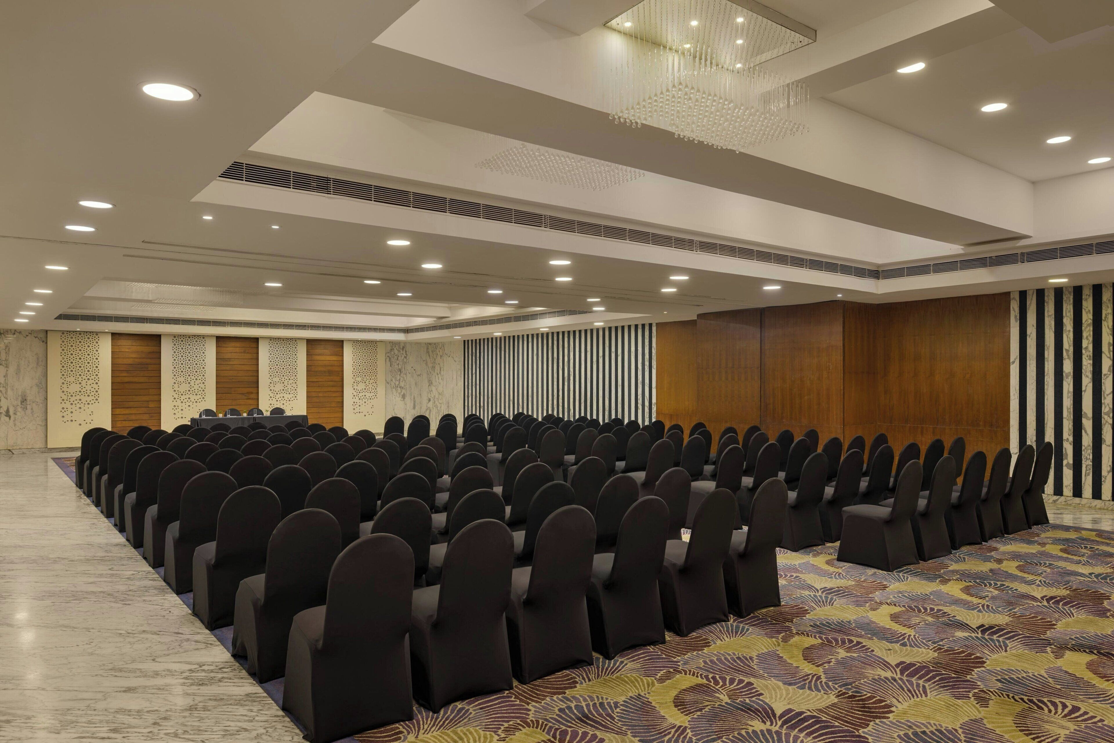 A conference room with rows of chairs, a patterned carpet, and a chandelier.