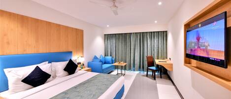 A modern hotel room with a large bed, a desk, a television, and a seating area.