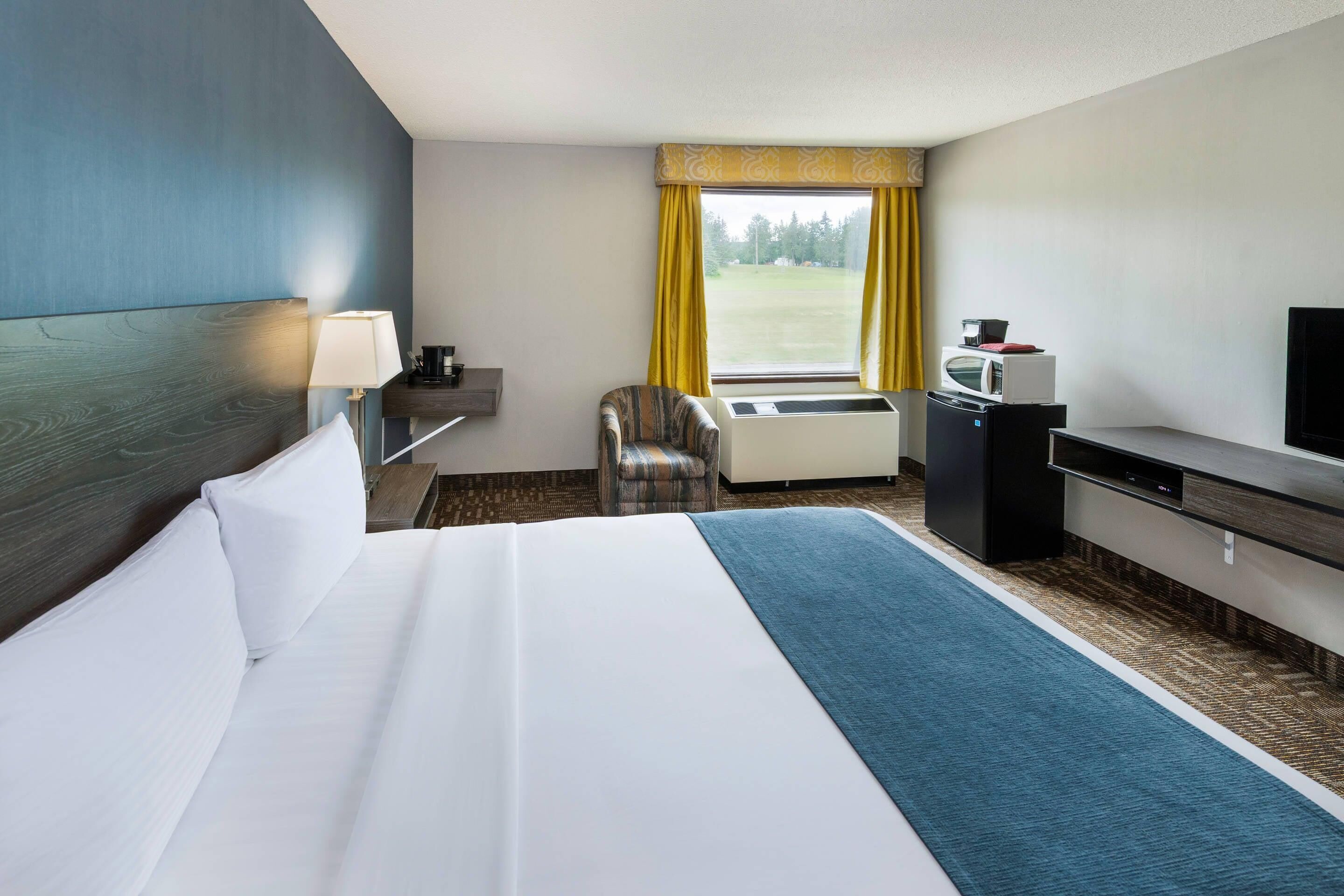 Een hotelkamer met een bed, een bureau, een stoel, een televisietoestel en een raam met gordijnen.