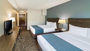 Habitación de hotel con dos camas, televisión y escritorio con lámpara.