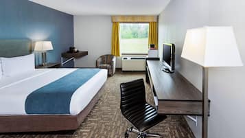 A hotel room with a bed, a desk with a television, a chair, a lamp, and a window with curtains.