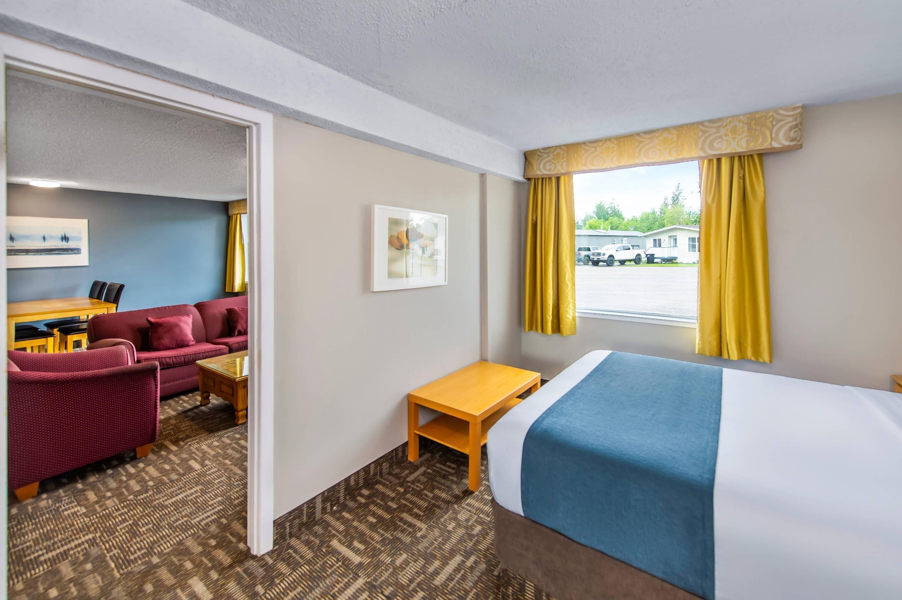 Habitación de hotel con cama, escritorio, sofá y una silla. Hay una ventana con cortinas y vista a un estacionamiento.