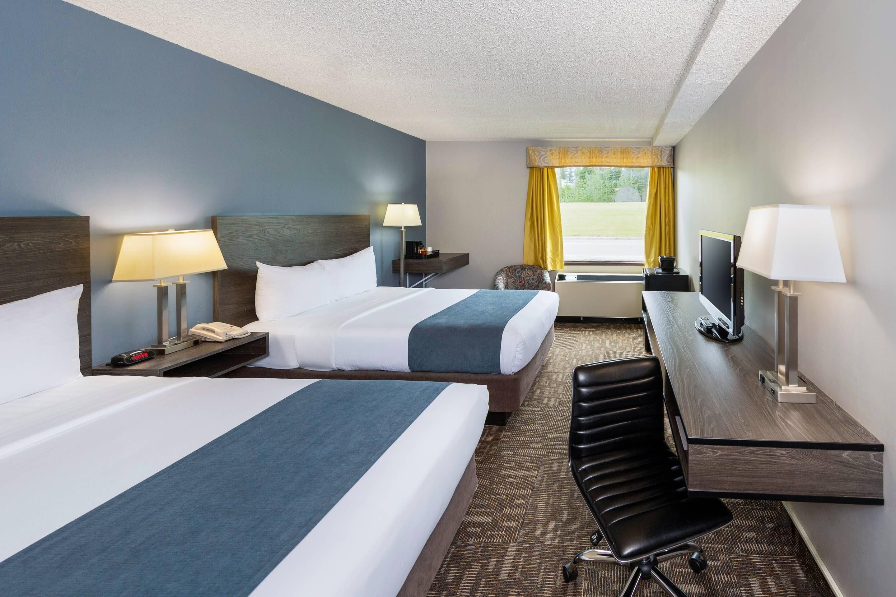 A hotel room with two beds, a desk, a chair, a TV, and a window with curtains.