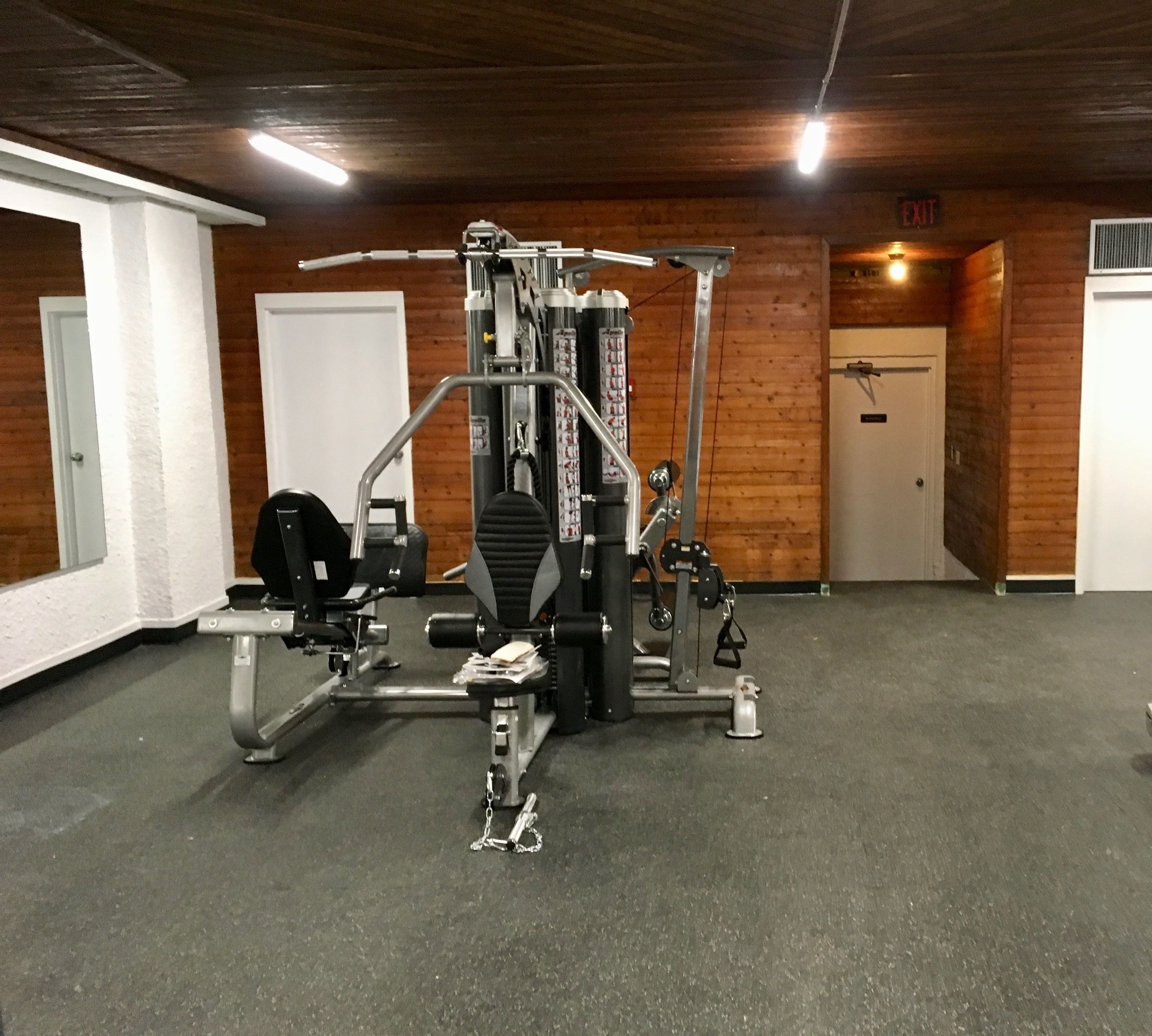 Un gimnasio con diferentes máquinas de ejercicio, una puerta blanca y paredes de madera.