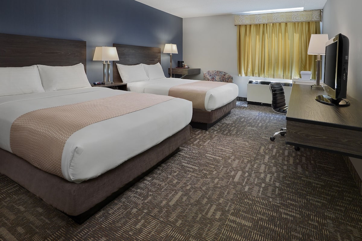 A hotel room with two beds, a desk with a computer, a TV, and a window with curtains.