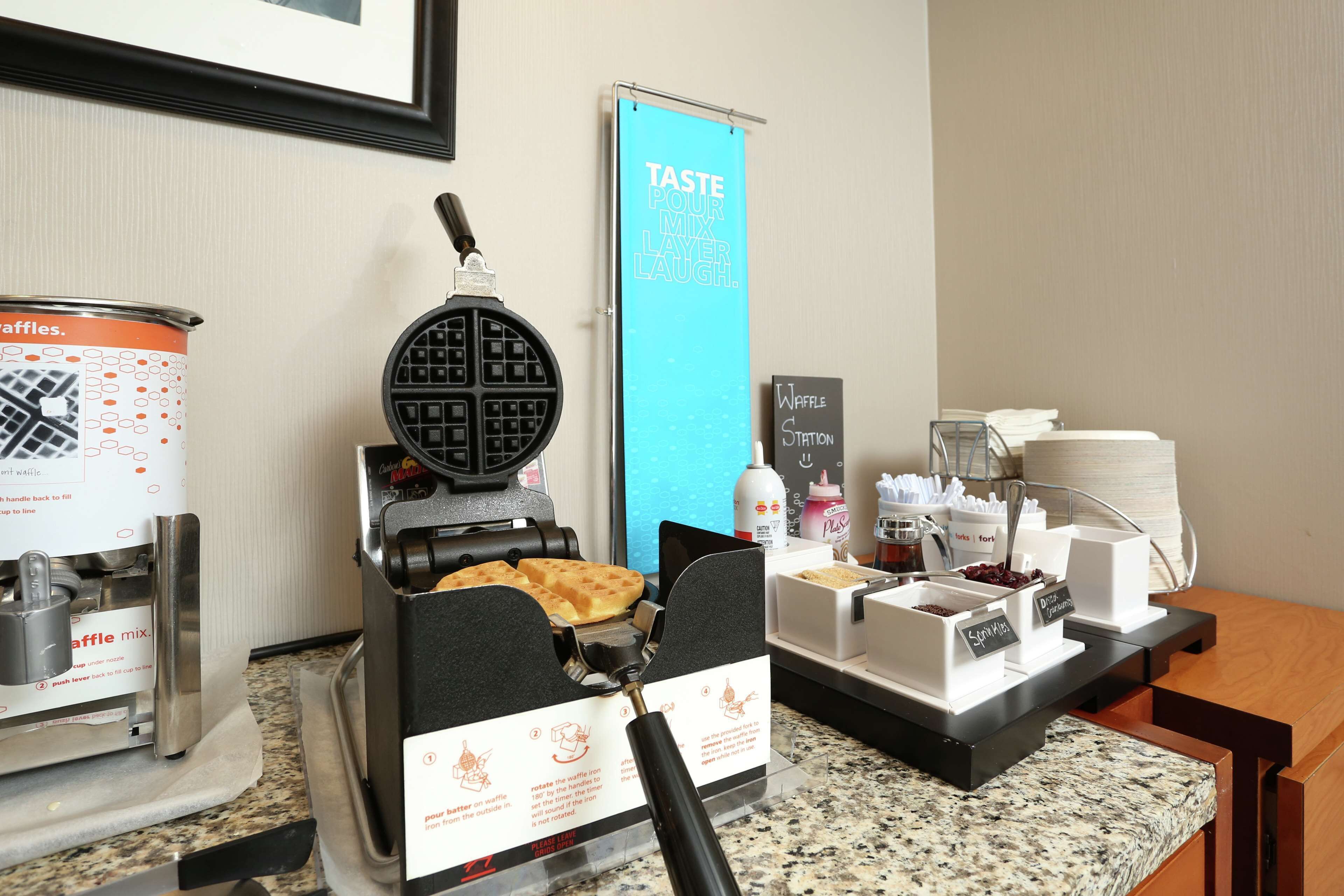 Una estación de gofres con una gofrera, un recipiente para la mezcla de gofres y un cartel que dice 'Waffle Station'.