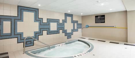 A swimming pool with a tiled mosaic design, a hot tub, and a sign indicating the pool's temperature range.