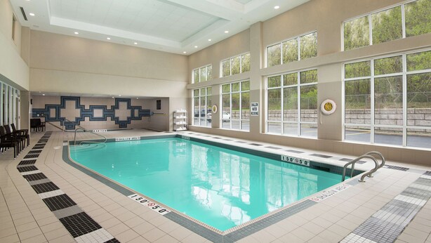 Piscina interior com pistas demarcadas, piso azulejado e vista para o exterior através de grandes janelas.